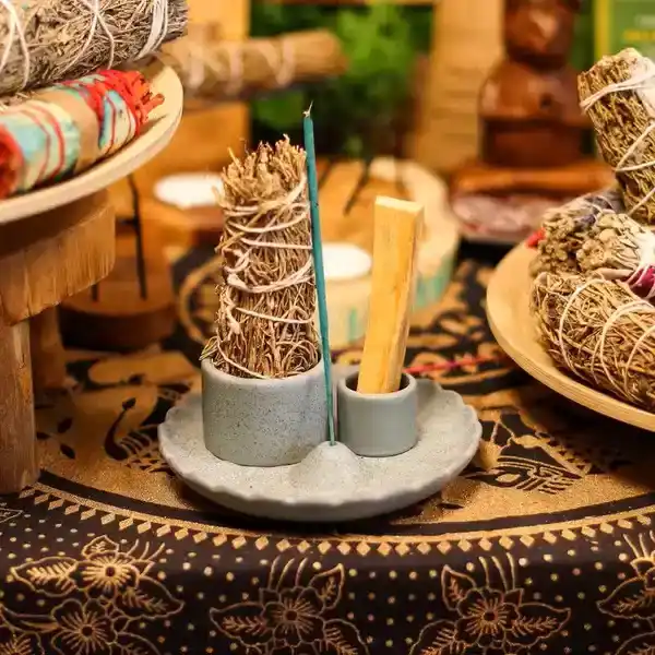 Ceramiczna niebieska podstawka w formie kwiatu lotosu z dwoma cylindrami na pęczki ziół oraz drewienka Palo Santo na ciemnym tle.