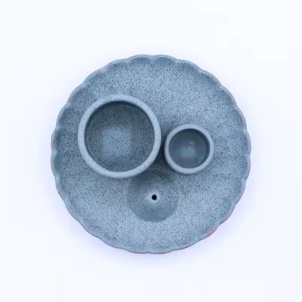 Ceramiczna niebieska podstawka w formie kwiatu lotosu z dwoma cylindrami na pęczki ziół oraz drewienka Palo Santo na ciemnym tle.