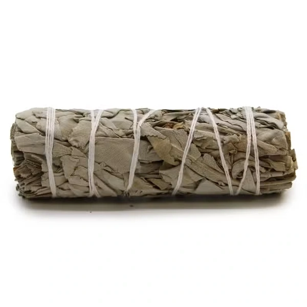 Zwarty pęczek suszonej białej szałwii o długości 10 cm związany naturalnym sznurkiem obok tlącego się liścia na ceramicznej podstawce.