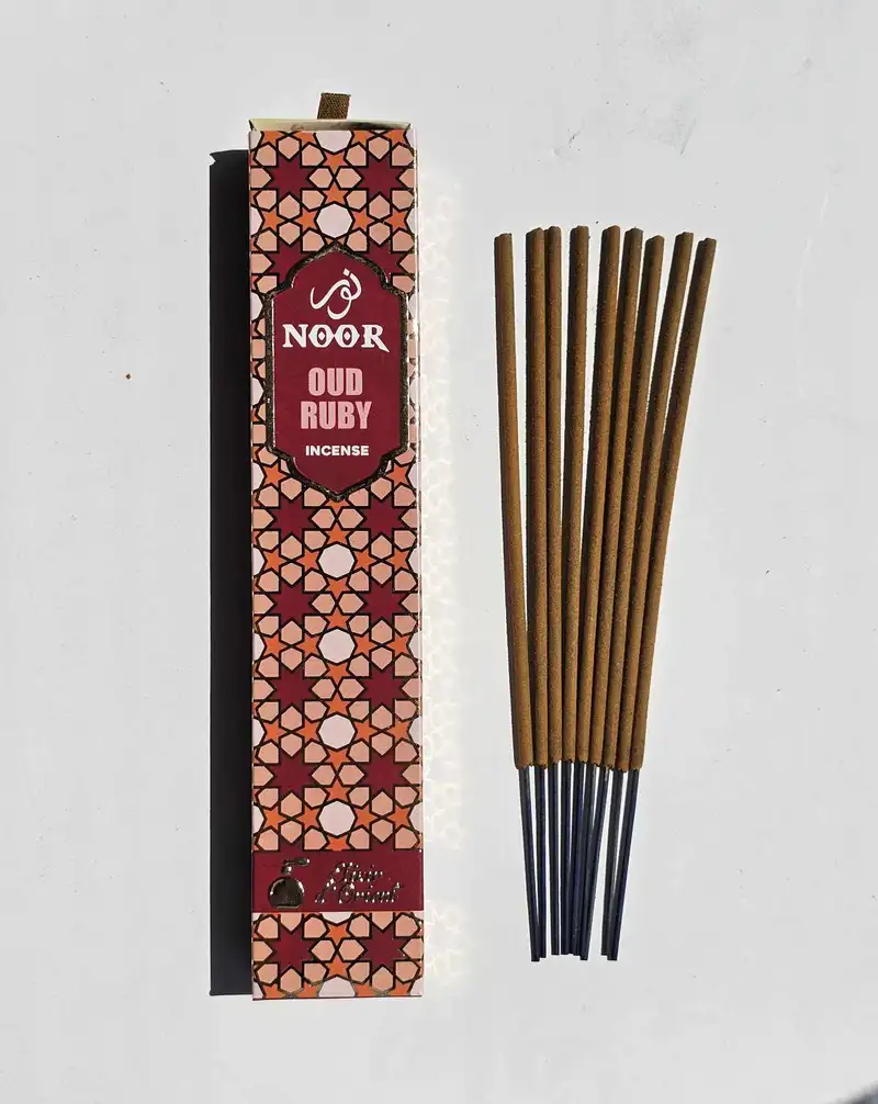 Eleganckie opakowanie kadzidełek premium NOOR Oud Ruby w głębokiej rubinowej oprawie obok grubych patyczków masala.