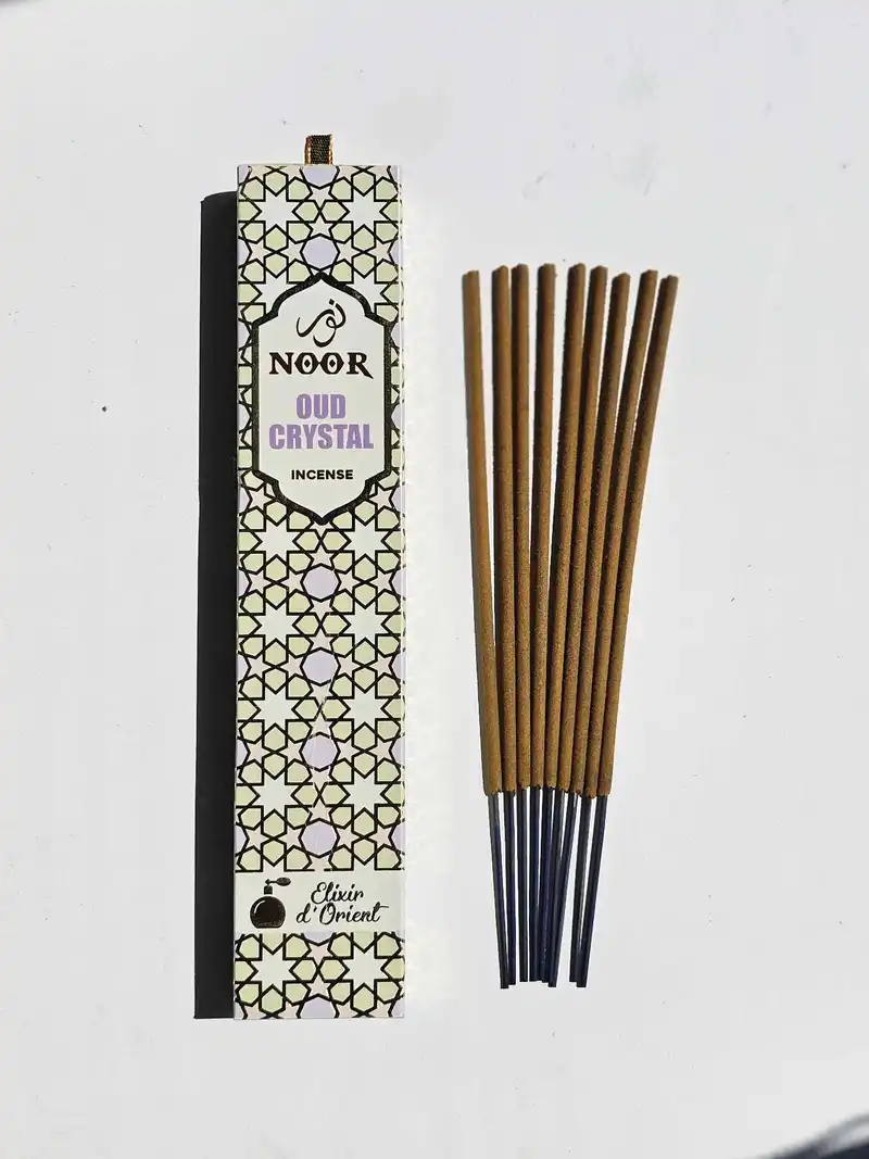 Eleganckie kremowe opakowanie kadzidełek premium NOOR Oud Crystal obok grubych patyczków masala.