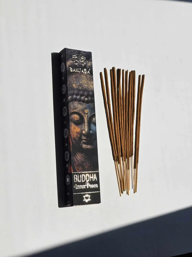 Oryginalne kamiennoszare opakowanie kadzidełek BANJARA Buddha Inner Peace ze złotym wizerunkiem Buddy obok naturalnych patyczków masala.