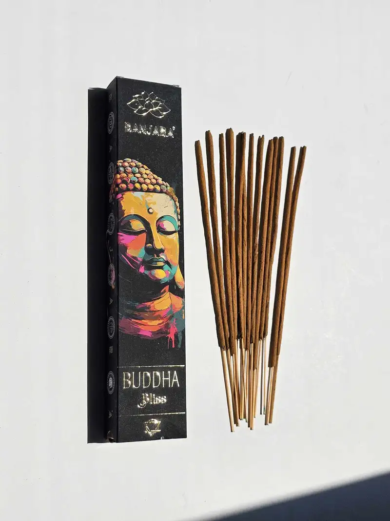 Oryginalne ciemne opakowanie kadzidełek BANJARA Buddha Bliss ze złotym portretem Buddy obok naturalnych patyczków masala.