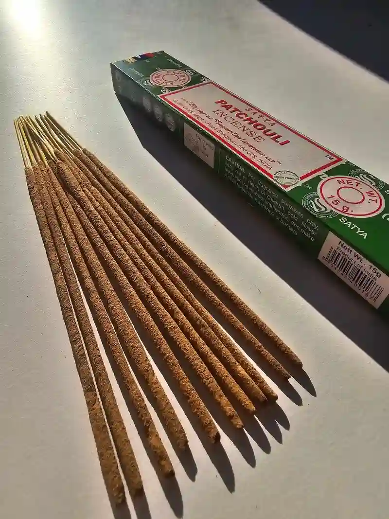 Oryginalne zielono kremowe opakowanie indyjskich kadzidełek SATYA Patchouli obok naturalnych patyczków masala.
