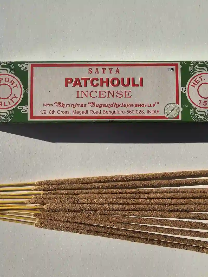 Oryginalne zielono kremowe opakowanie indyjskich kadzidełek SATYA Patchouli obok naturalnych patyczków masala.