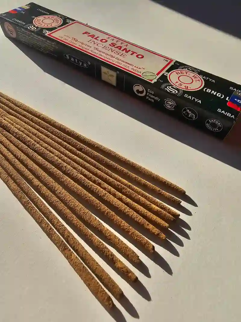 Oryginalne granatowo kremowe opakowanie indyjskich kadzidełek SATYA Palo Santo obok naturalnych patyczków masala.