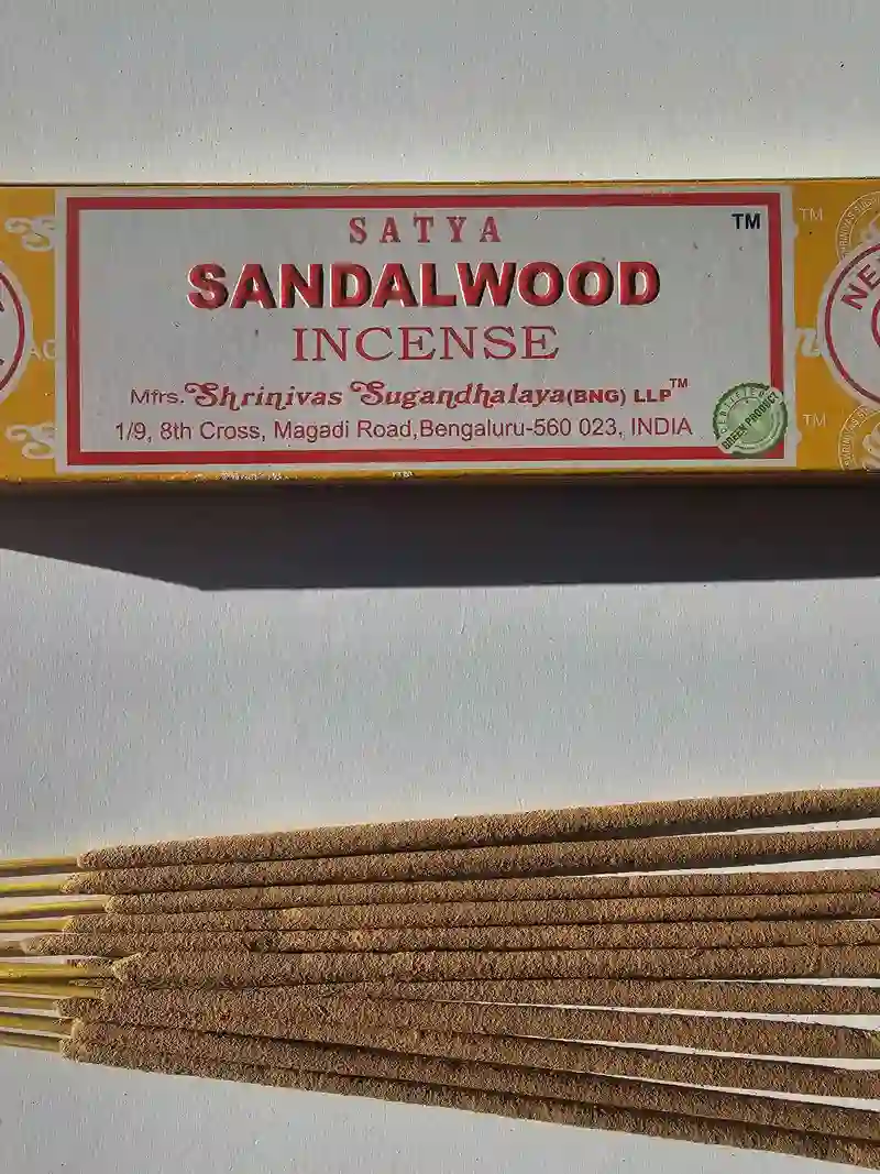 Oryginalne pomarańczowo kremowe opakowanie indyjskich kadzidełek SATYA Sandalwood obok naturalnych patyczków masala.