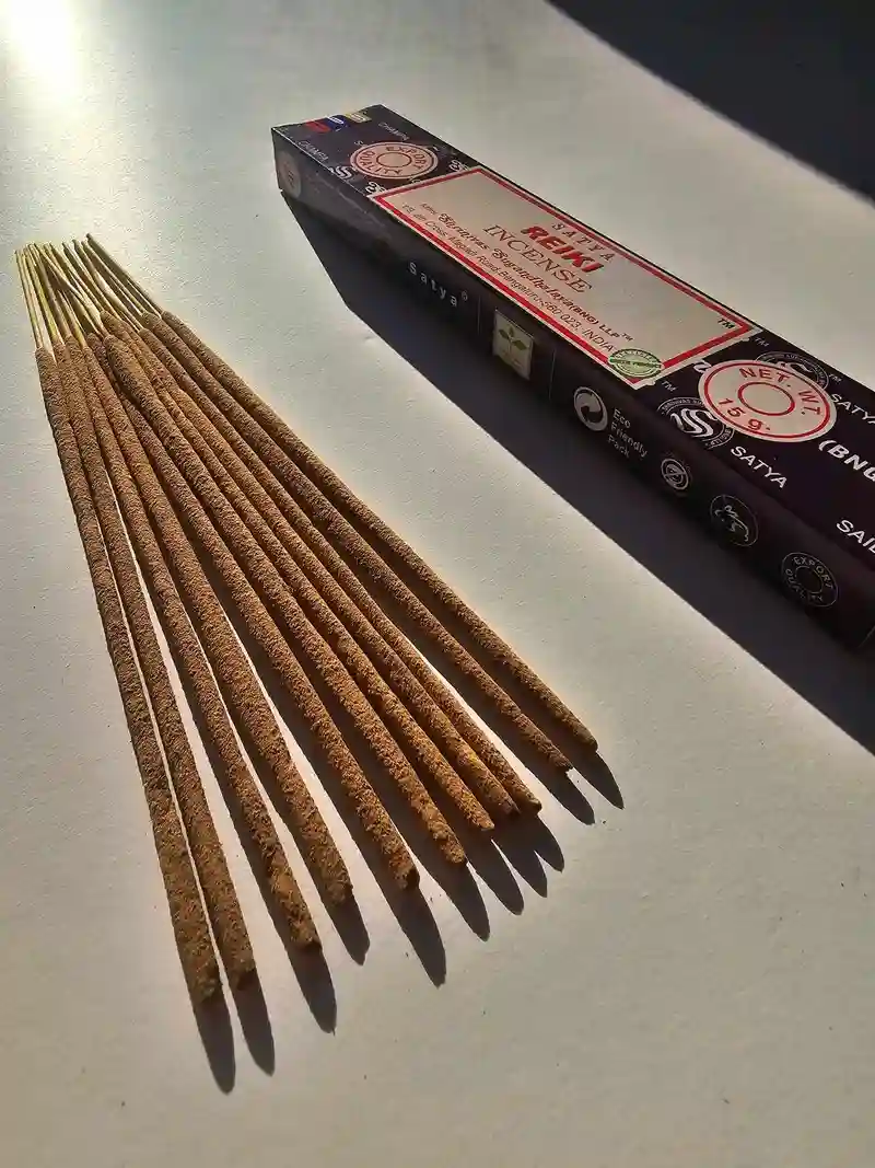 Oryginalne bordowo kremowe opakowanie indyjskich kadzidełek SATYA Reiki obok naturalnych patyczków masala.