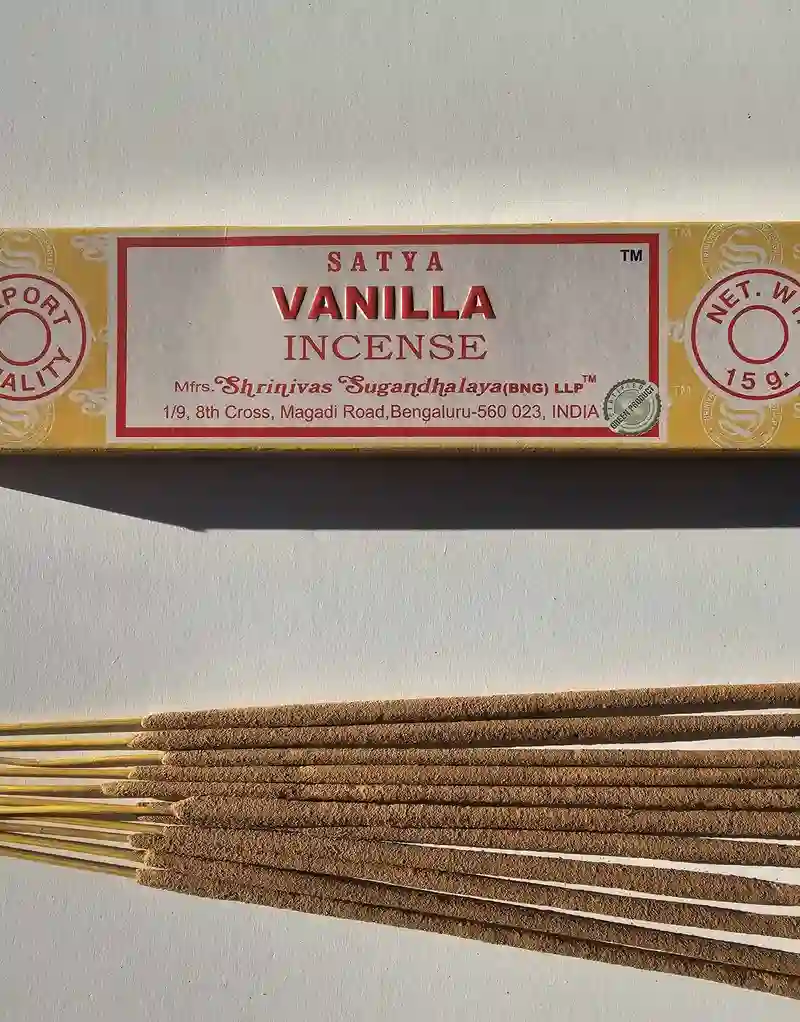 Oryginalne żółto kremowe opakowanie indyjskich kadzidełek SATYA Vanilla obok naturalnych patyczków masala.