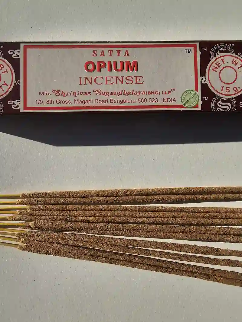 Oryginalne ciemnobrązowo kremowe opakowanie indyjskich kadzidełek SATYA Opium obok naturalnych patyczków masala.