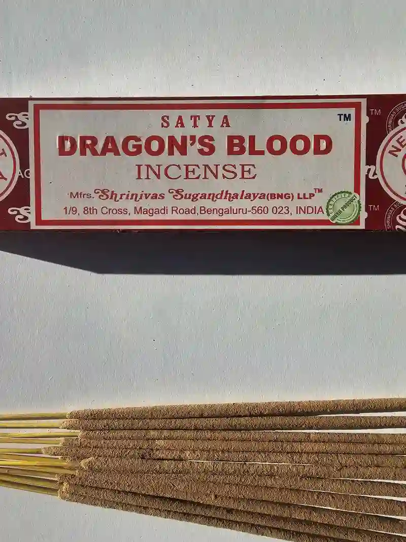 Oryginalne bordowo kremowe opakowanie indyjskich kadzidełek SATYA Dragon's Blood obok naturalnych patyczków masala.