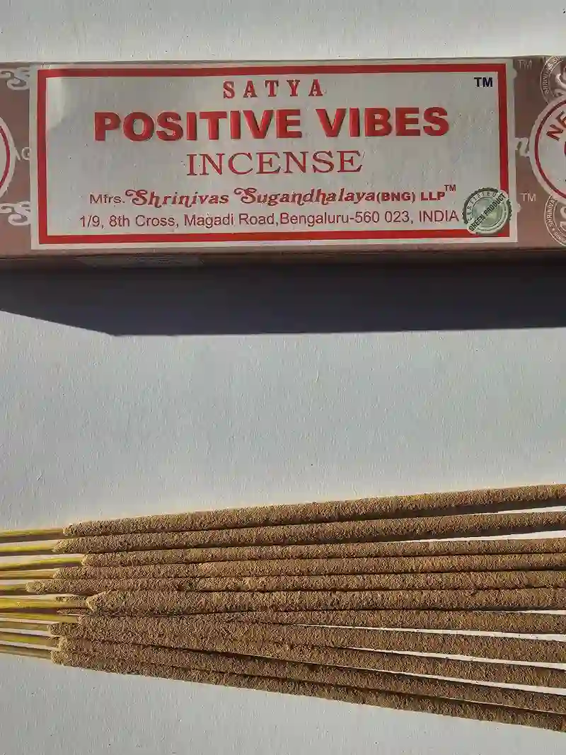 Oryginalne pomarańczowo kremowe opakowanie indyjskich kadzidełek SATYA Positive Vibes obok naturalnych patyczków masala.