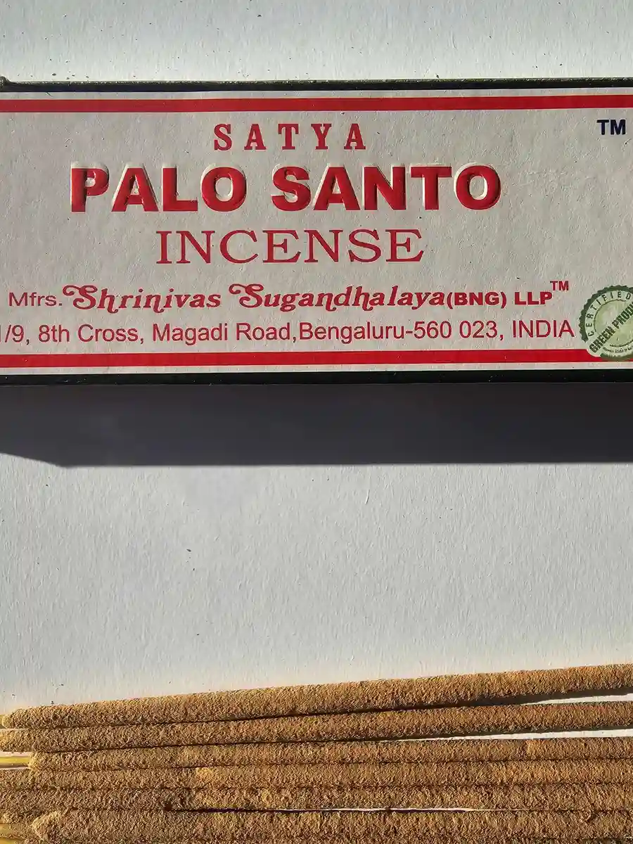 Kadzidła Satya White Sage 15g w jasnoszarym kartonowym pudełku, pod którym leży kilkanaście patyczków z jasnobrązową masalą na białym tle z mocnym cieniem.