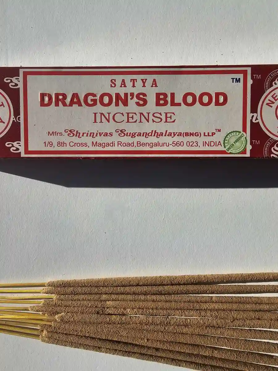 Czerwone pudełko kadzideł Satya Dragon's Blood 15g leżące nad grupą jasnobrązowych patyczków na białym tle z wyraźnym, ostrym cieniem.