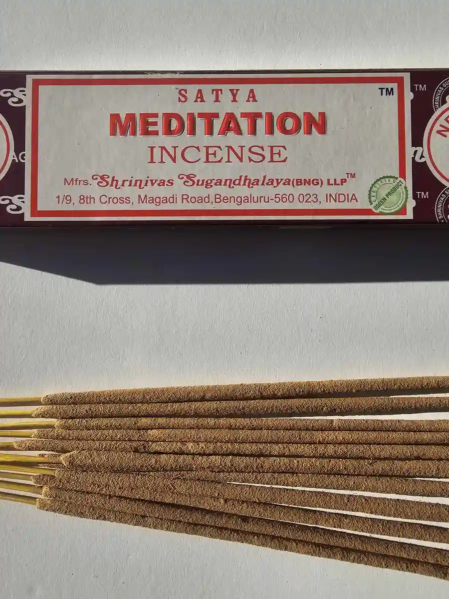 Bordowe pudełko kadzideł Satya Meditation 15g leżące nad stosem jasnobrązowych patyczków na białym tle z wyraźnym cieniem rzucanym w prawą stronę.