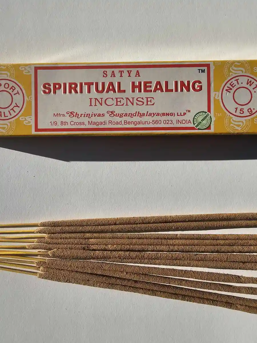 Jasnożółte pudełko kadzideł Satya Spiritual Healing 15g ułożone poziomo nad grupą jasnobrązowych patyczków na białym tle z wyraźnym, ostrym cieniem.