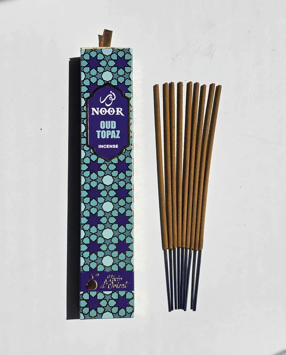 Lazurowe opakowanie kadzideł Noor Oud Topaz na eleganckim tle, prezentujące rozwiązanie dla osób pragnących otoczyć się aurą sukcesu i obfitości.