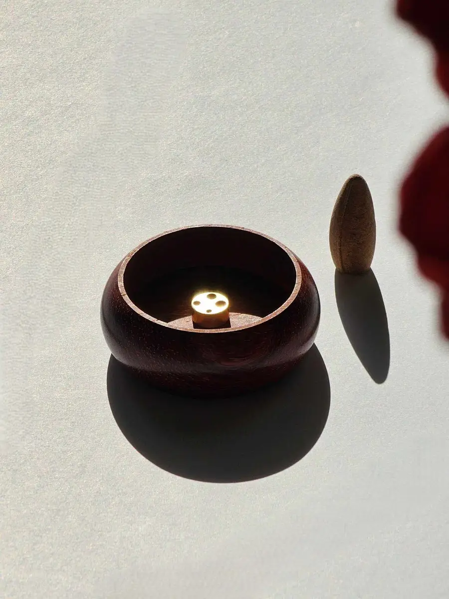 Mała, drewniana podstawka w dłoni, pokazująca jej kompaktowy rozmiar i przeznaczenie wyłącznie do kadzideł stożkowych.