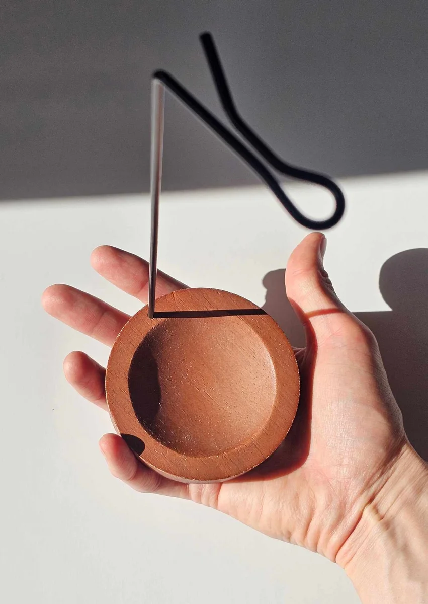 Elegancki metalowy uchwyt trzymający kadzidło patyczkowe do góry nogami nad drewnianą podstawką, prezentujący nowoczesny sposób palenia bez rozsypywania popiołu.