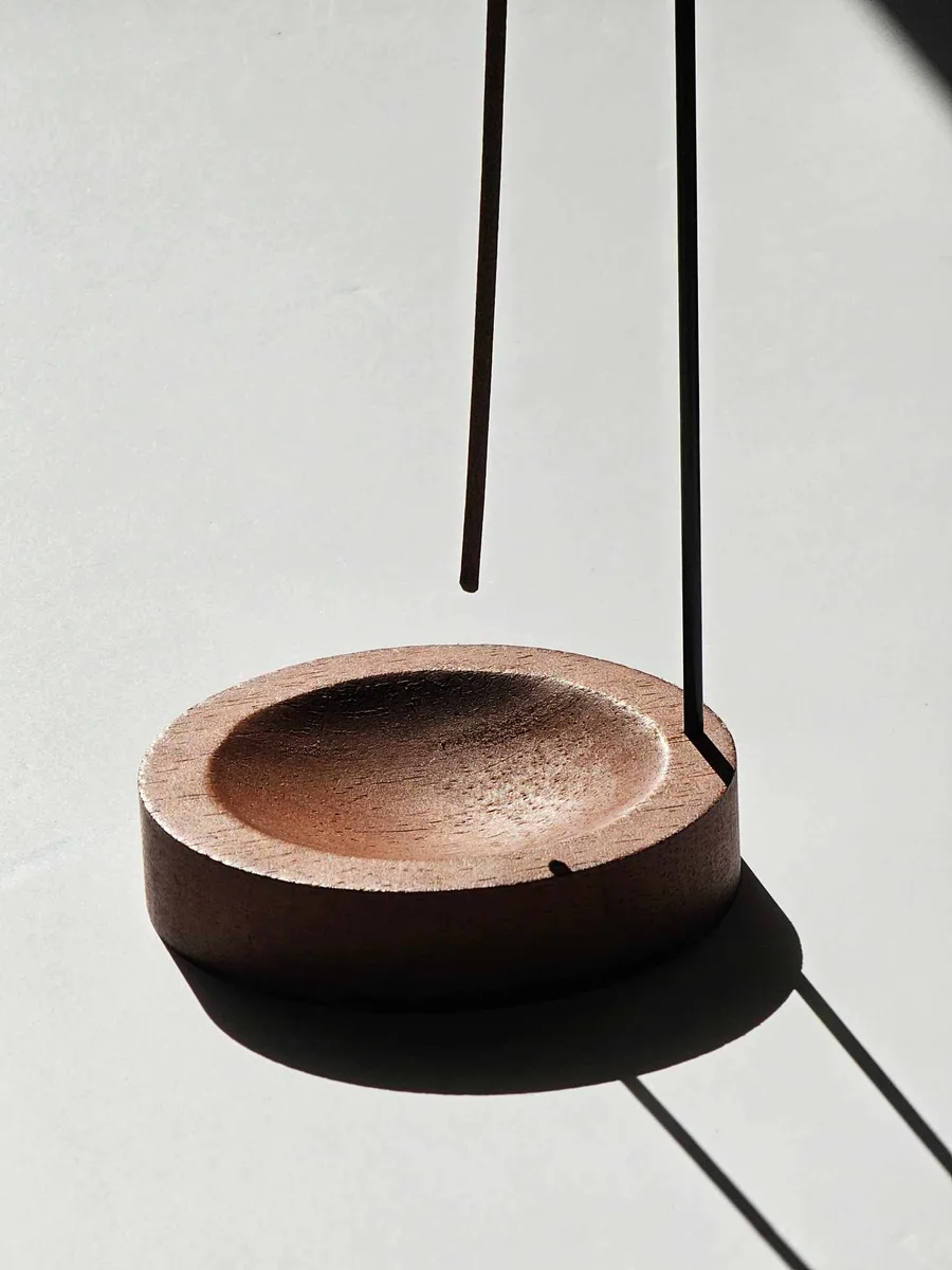 Elegancki metalowy uchwyt trzymający kadzidło patyczkowe do góry nogami nad drewnianą podstawką, prezentujący nowoczesny sposób palenia bez rozsypywania popiołu.