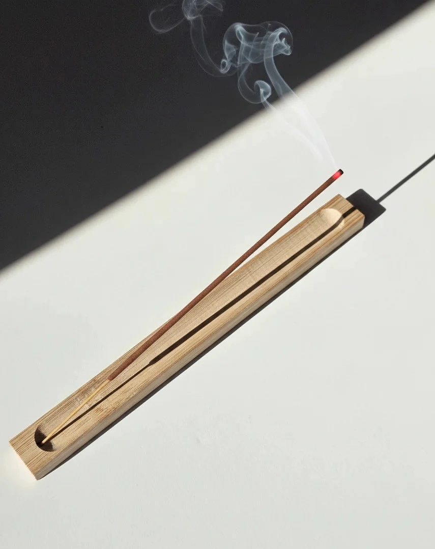 Wąska bambusowa podstawka typu korytko z zapalonym kadzidłem, umieszczona na jasnym blacie, podkreślająca minimalistyczny design.