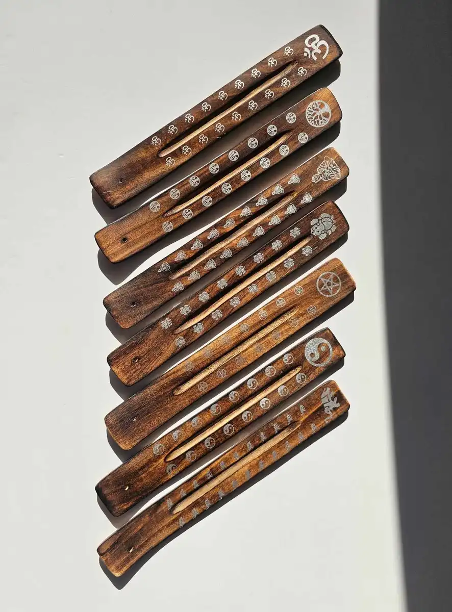 Zestaw drewnianych podstawek typu narta w ciemnym kolorze z różnymi białymi zdobieniami (Om, drzewo życia, yin-yang), prezentujący różnorodność dostępnych wzorów.
