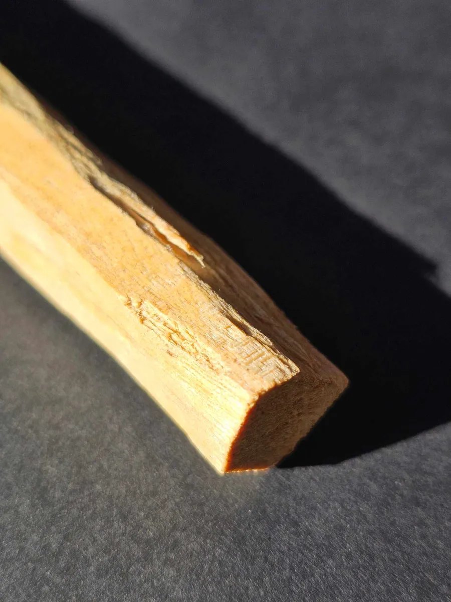 Pojedyncza szczapka naturalnego Palo Santo na ciemnym tle, oświetlona profesjonalnym, punktowym światłem.